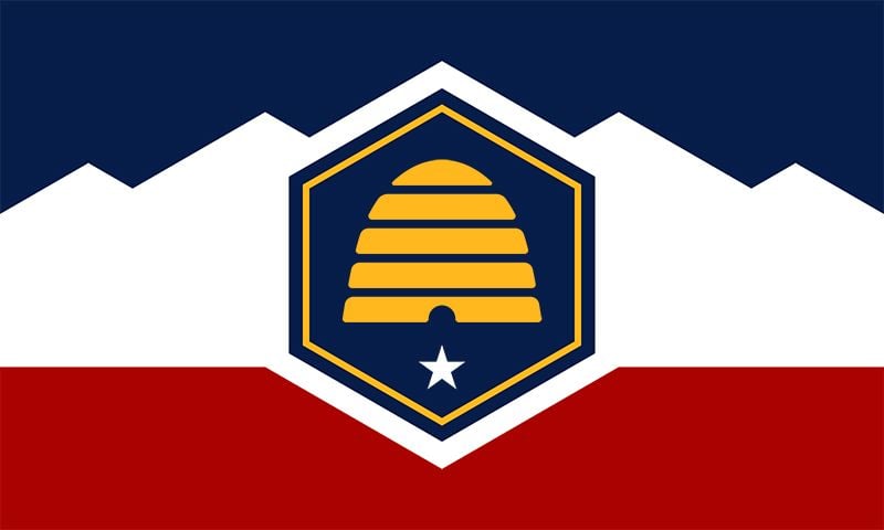 A flag design featuring a yellow beehive within a blue hexagon, a white star below, and a background of blue, white, and red with mountain shapes.
