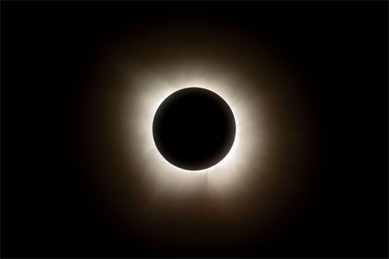 A total solar eclipse showing a dark circle (the Moon) obscuring the Sun, surrounded by the Sun's glowing white corona against a black sky.